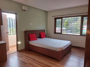 a bedroom with a bed with two red pillows on it at Nidha Home in Ooty