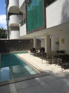 una piscina con sillas y una mesa en un edificio en Apartamento Capitães de Areia Ilheus, en Ilhéus
