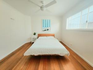 a bed in a white room with a wooden floor at Beachfront Mid Coast Escape in Seaford +14 photos