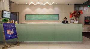 a woman sitting at a green counter in a lobby at Jinjiang Inn Baotou Donghe East Railway Station in Baotou