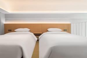 two beds in a room with white sheets at Chenfeng Hotel Wuhan Baishazhou Longhu Tianjie Branch in Wuhan