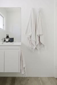 a white bathroom with white towels hanging on a wall at Medona - Narrawallee Beach House in Narrawallee