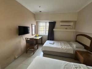 a hotel room with two beds and a desk and a television at Angsa Hotel in Seremban