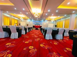 Un salón de banquetes con sillas blancas y una alfombra roja. en Sindoro Hotel Cilacap By Conary, en Cilacap