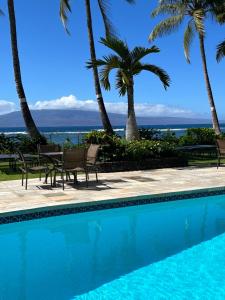 a swimming pool with palm trees and a view of the ocean at Compass Blue Lahaina in Lahaina