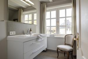 a white bathroom with a sink and a chair at Leo in Keitum +43 photos