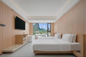 ein Schlafzimmer mit einem großen weißen Bett und einem Flachbildfernseher in der Unterkunft Shuitiao Boli Hotel (Yangshuo Shili Gallery Yulonghe Branch) in Gaotian