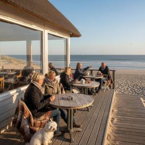a group of people sitting at tables on the beach at Stylish Suite Steps To Shore in Zoutelande
