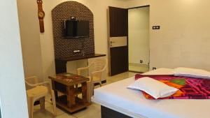 a room with a bed and a table and a television at Hotel Prathamesh in Panchgani