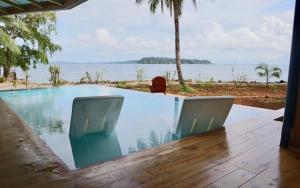 a swimming pool with two chairs next to the water at Bocas Beachfront Lodge Spacious Corner King Suite Ocean View Sand Level in Bocas del Toro