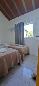 two beds in a white room with a window at Casa em Porto de Galinhas - PRIVÊ DAS ONDAS in Porto De Galinhas