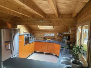 La cuisine est équipée de placards orange et d'un réfrigérateur en acier inoxydable. dans l'établissement Villa Aurora, à Labaroche