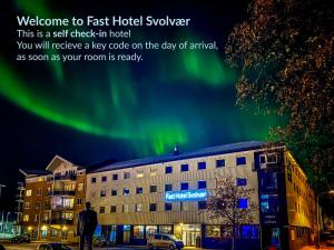 a man standing in front of a building with the northern lights at Fast Hotel Svolvær in Svolvær