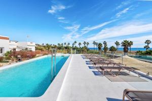 une piscine avec des chaises et l'océan en arrière-plan dans l'établissement Templo Sotogrande, à Sotogrande