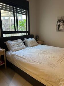 a bed with white sheets and pillows in a bedroom at Garden apartment in Ramat HaSharon in Ramat Hash Sharon