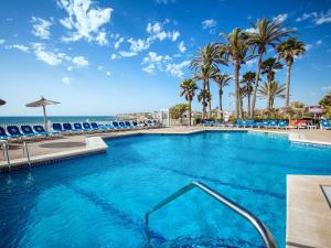 a swimming pool with palm trees and the ocean at Hotel Servigroup La Zenia in Playas de Orihuela
