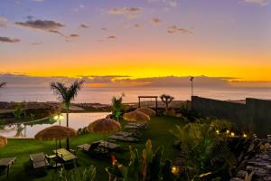 un coucher de soleil sur un complexe hôtelier avec des chaises et des parasols dans l'établissement Experiencia Habitación Burbuja con Jacuzzi Privado, Piscina y Vistas al Mar, à Guía de Isora