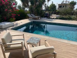 a swimming pool with two chairs and a table next to it at Villa Leda - The Guest Wing in Paphos City