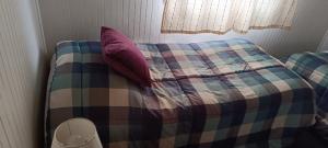 a bed with a plaid blanket and pillows at Cabaña Quemchi in Quemchi
