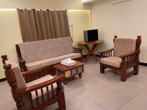 ein Wohnzimmer mit zwei Stühlen und einer Couch und einem Fernseher in der Unterkunft Vishnu VAASAM Serviced Apartment Srirangam in Tiruchchirāppalli