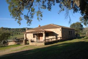 a stone house in a field with a tree at Casa Rural La Vega Piscina, naturaleza y vistas in San Vicente de Alcántara