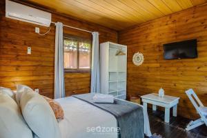een slaapkamer met houten wanden en een bed met een televisie bij Chalés Elegantes e Completos em Imbituba - REL in Praia do Rosa
