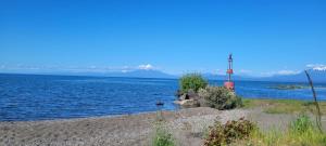 a large body of water with a lighthouse on the shore at Cabaña interior en el centro de llanquihue in Llanquihue