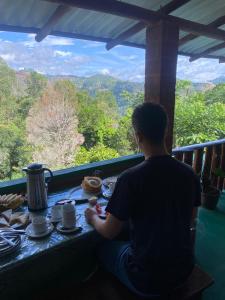 un homme assis à une table, regardant les montagnes dans l'établissement NETHSARA cottage, à Ella