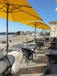 Una fila de mesas y sillas con sombrillas en la playa. en Hôtel The Originals Miramar, Royan Pontaillac, en Royan