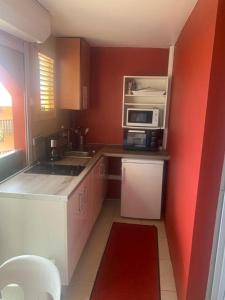 Una pequeña cocina con paredes rojas y un microondas en Studio Papaye - confort et calme près des plages, en Sainte-Anne