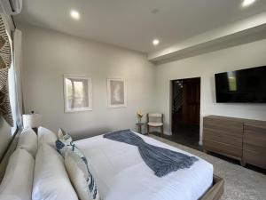 a bedroom with a white bed and a tv at Emerald Blue Villa - Modern 2BR Villa with Rooftop Lounge Pool in Placencia Village