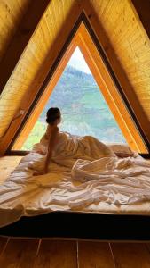 Eine Frau, die auf einem Bett vor einem Fenster sitzt. in der Unterkunft warm house - sunrise merisi in Merisi