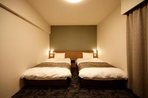 two beds in a small room with two lamps at Dormy Inn Nagano in Nagano