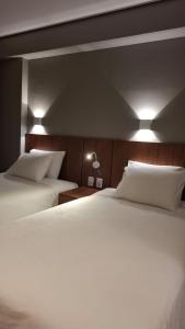 a bedroom with two beds and two lights on the wall at Hotel C jaguariuna in Jaguariúna
