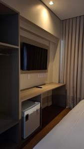 Una habitación con televisión y un escritorio con una cama. en Hotel C jaguariuna, en Jaguariúna