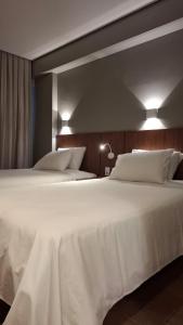 1 dormitorio con 2 camas, sábanas blancas y luces en Hotel C jaguariuna, en Jaguariúna