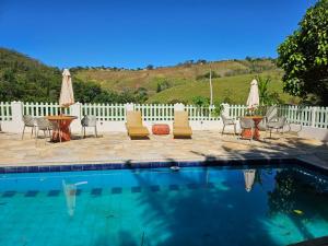a swimming pool with chairs and a table and umbrellas at Villa Sol hospedaria in Paty do Alferes