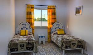 a bedroom with two beds with yellow curtains and a window at Djerba Dar Iyad in Mezraya