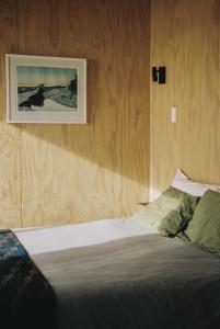 a bedroom with a bed with a picture on the wall at The Huts in Ahipara