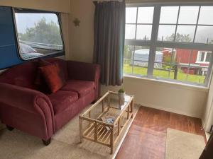 ein Wohnzimmer mit einem roten Sofa und einem Tisch in der Unterkunft Simple Cabin, Kuaotunu - Peaceful, Affordable Stay in Kuaotunu + 2 Fotos