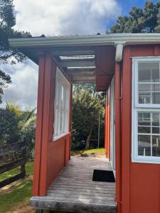 ein rotes Haus mit einer Veranda und einer Tür in der Unterkunft Simple Cabin, Kuaotunu - Peaceful, Affordable Stay in Kuaotunu