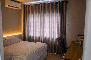 een slaapkamer met een bed en een raam met gordijnen bij Apartamento 1 Quarto Canasvieiras in Florianópolis