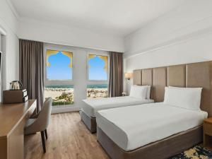 a hotel room with two beds and a desk and two windows at Rixos Bab Al Bahr - Ultra All Inclusive in Ras al Khaimah