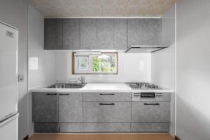 eine Küche mit grauen Schränken, einem Waschbecken und einem Fenster in der Unterkunft Landmark Annex in Furano