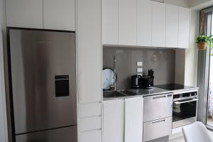 une cuisine avec des armoires blanches et un réfrigérateur en acier inoxydable dans l'établissement CBD luxury Apartments Union green with Skytower View, à Auckland