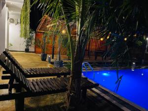 eine Holzbank neben einem Pool mit einer Palme in der Unterkunft Indunil place hiriketiya in Dikwella