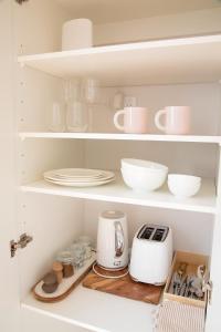 a kitchen with white shelves with dishes and a toaster at The Coconut Hut Papamoa Beach in Tauranga