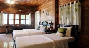 two beds in a room with wooden walls and windows at Ban Noi Resort Phrae in Sop Sai