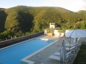 a pool with chairs and an umbrella next to a mountain at Quinta dos Castanheiros - Turismo Rural in Negreda