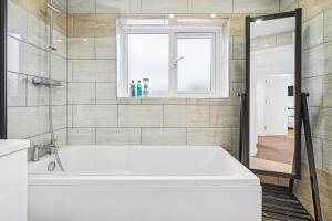 une baignoire blanche dans une salle de bains avec fenêtre dans l'établissement Windrush Court, The Spacious & Comfy 3BR House By AltoLuxo Short Lets & Serviced Accommodation With Free WiFi & Parking, à Thornbury